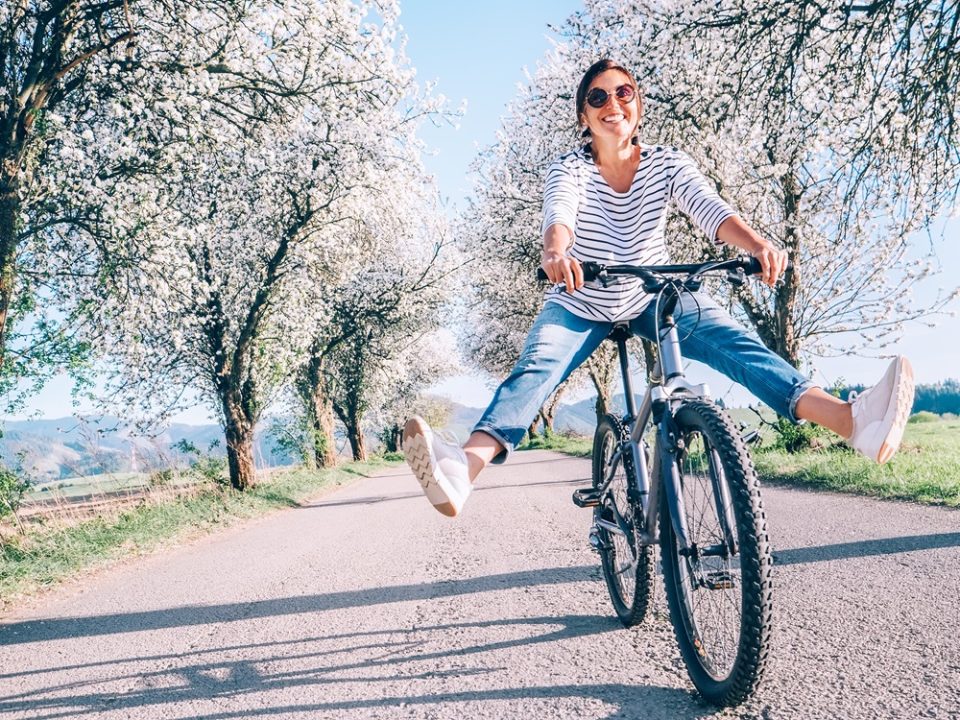 Mujer sonriente disfrutando de un paseo en bicicleta entre árboles florecidos, simbolizando articulaciones saludables