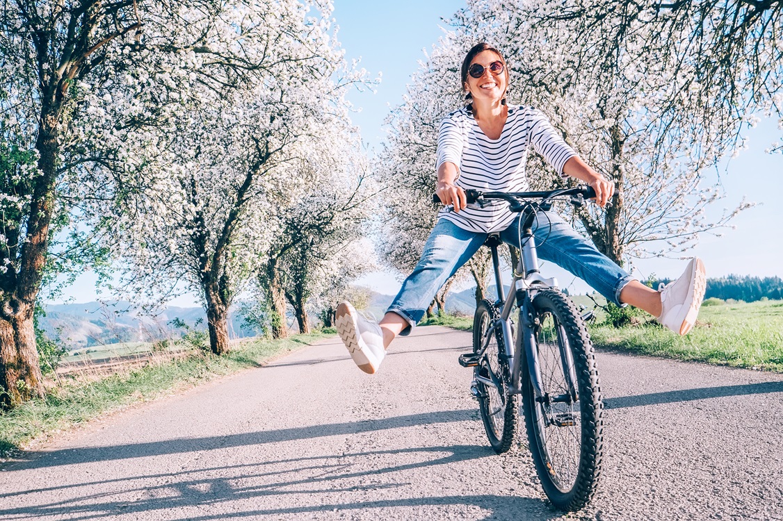 Mujer sonriente disfrutando de un paseo en bicicleta entre árboles florecidos, simbolizando articulaciones saludables